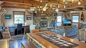 A rustic interior with a stone fireplace, wooden ceiling beams, and a large wooden dining table.