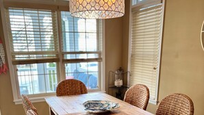 Ein Esszimmer mit Holztisch und Korbstühlen, einem gemusterten Teppich und einer hängenden Leuchte.