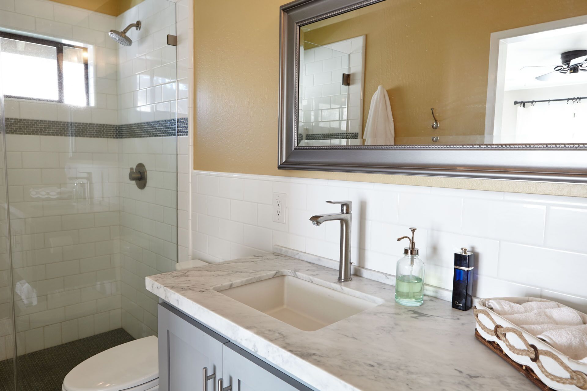 A bathroom with a glass shower enclosure, a sink with a marble countertop, and a mirror above the sink.