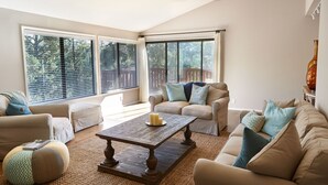 A spacious living room with a high ceiling fan, large windows with blinds, a beige sofa set, a wooden coffee table, and a decorative vase. - Charm and Modern Luxury in Heart of Wine Country (Sonoma)