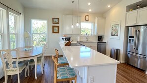 A modern kitchen with white cabinetry, a central island, wooden flooring, and pendant lighting.