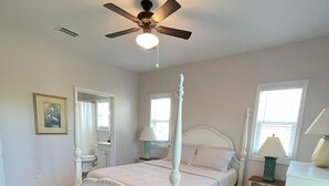 A bedroom with a four-poster bed, a ceiling fan, and a nightstand with a lamp.