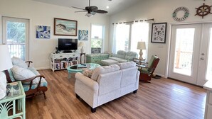 A spacious living room with hardwood floors, a ceiling fan, and a television.