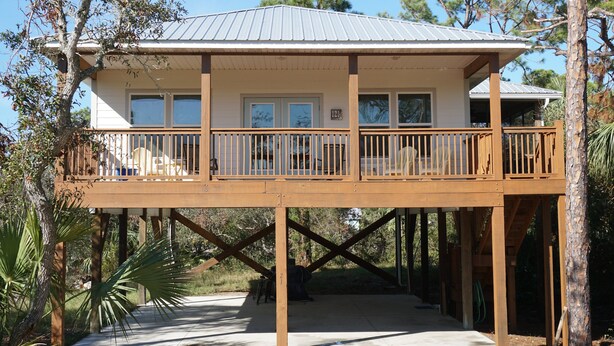 A two-story wooden structure with a balcony, supported by wooden pillars, surrounded by trees.
