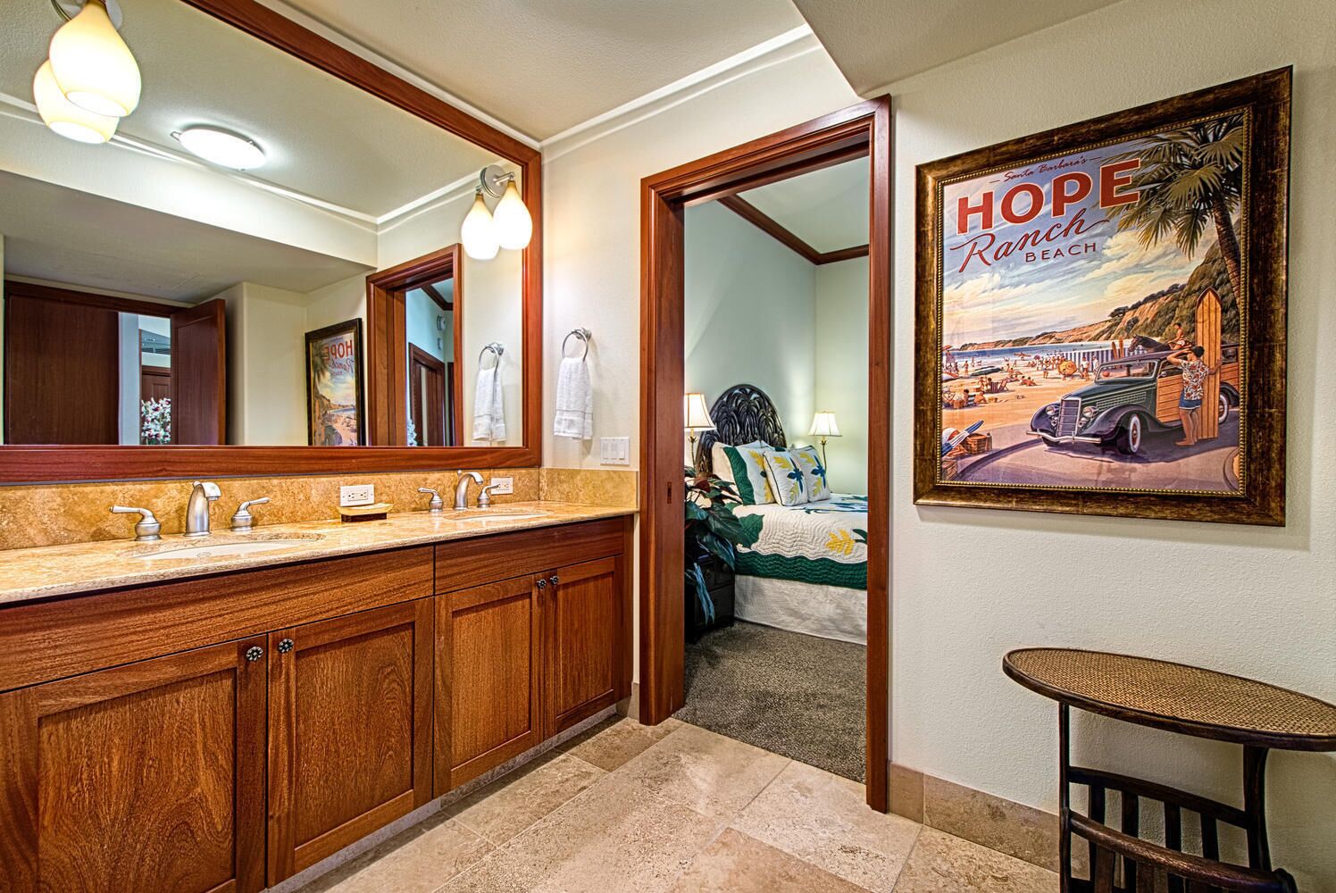 A hotel bathroom with wooden cabinets, a large mirror, and a framed picture of Hope Ranch Beach.