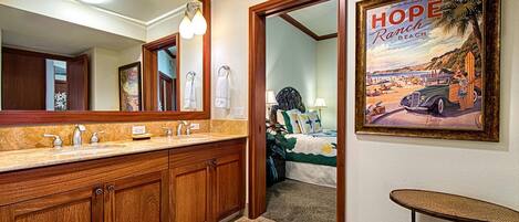 A hotel bathroom with wooden cabinets, a large mirror, and a framed picture of Hope Ranch Beach.