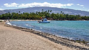 A beach with a boat, palm trees, and mountains in the background. - Paradise Awaits! Gorgeous Kolea Condo with Great Views (Waikoloa)