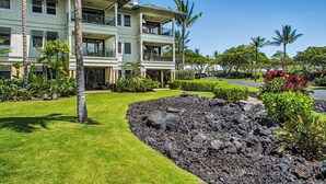 A multi-story hotel with a well-maintained lawn, a rock garden, and tropical plants. - Paradise Awaits! Gorgeous Kolea Condo with Great Views (Waikoloa)