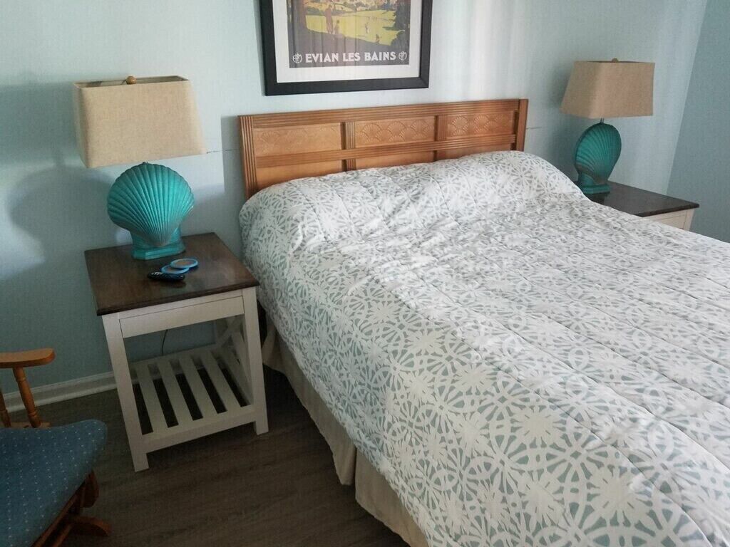 A neatly made bed with a patterned bedspread, two bedside tables with lamps, and a framed picture on the wall.