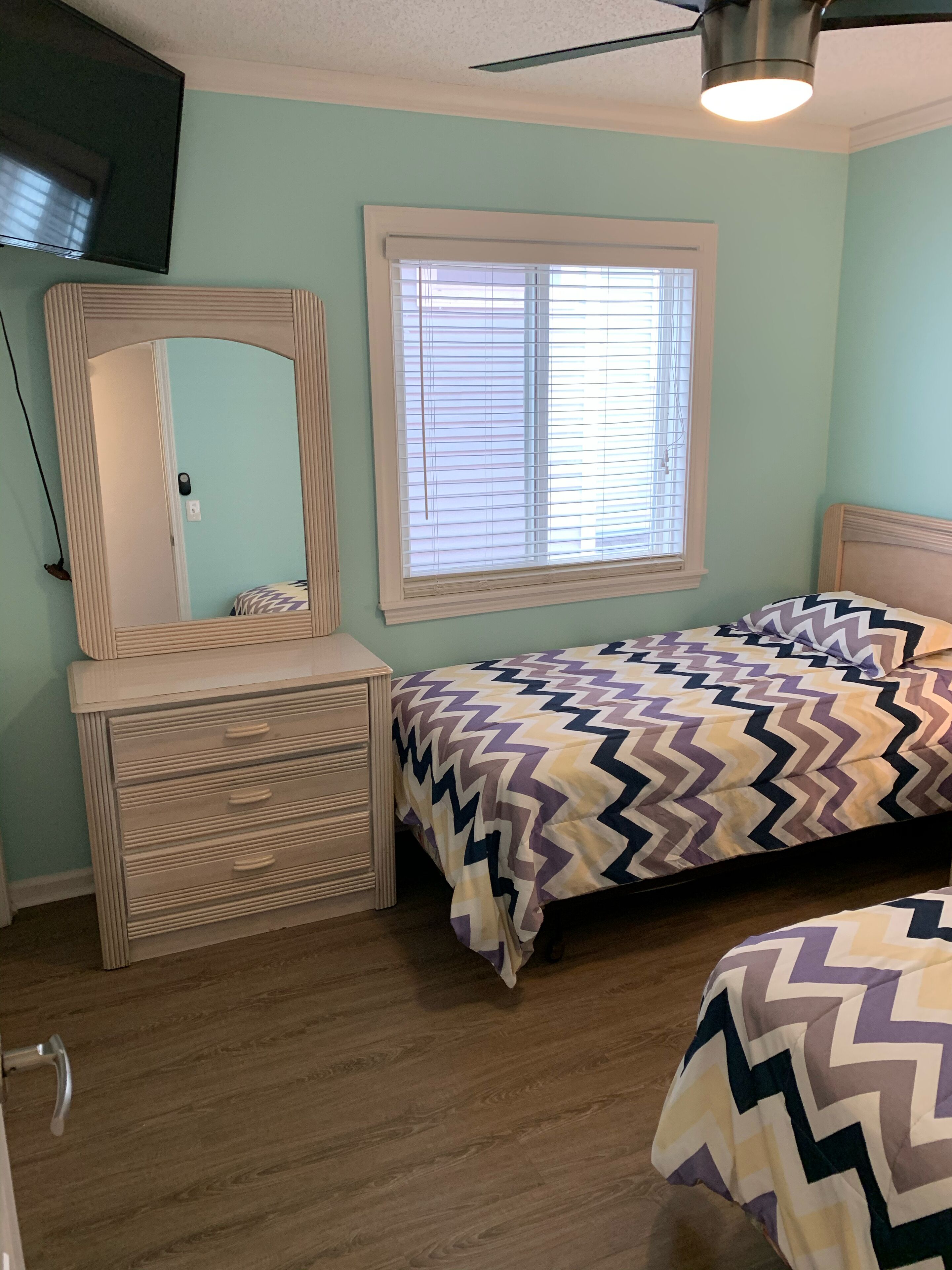 Quarto com cama, penteadeira, espelho e janela com persianas.