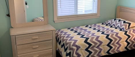 Quarto com cama, penteadeira, espelho e janela com persianas.