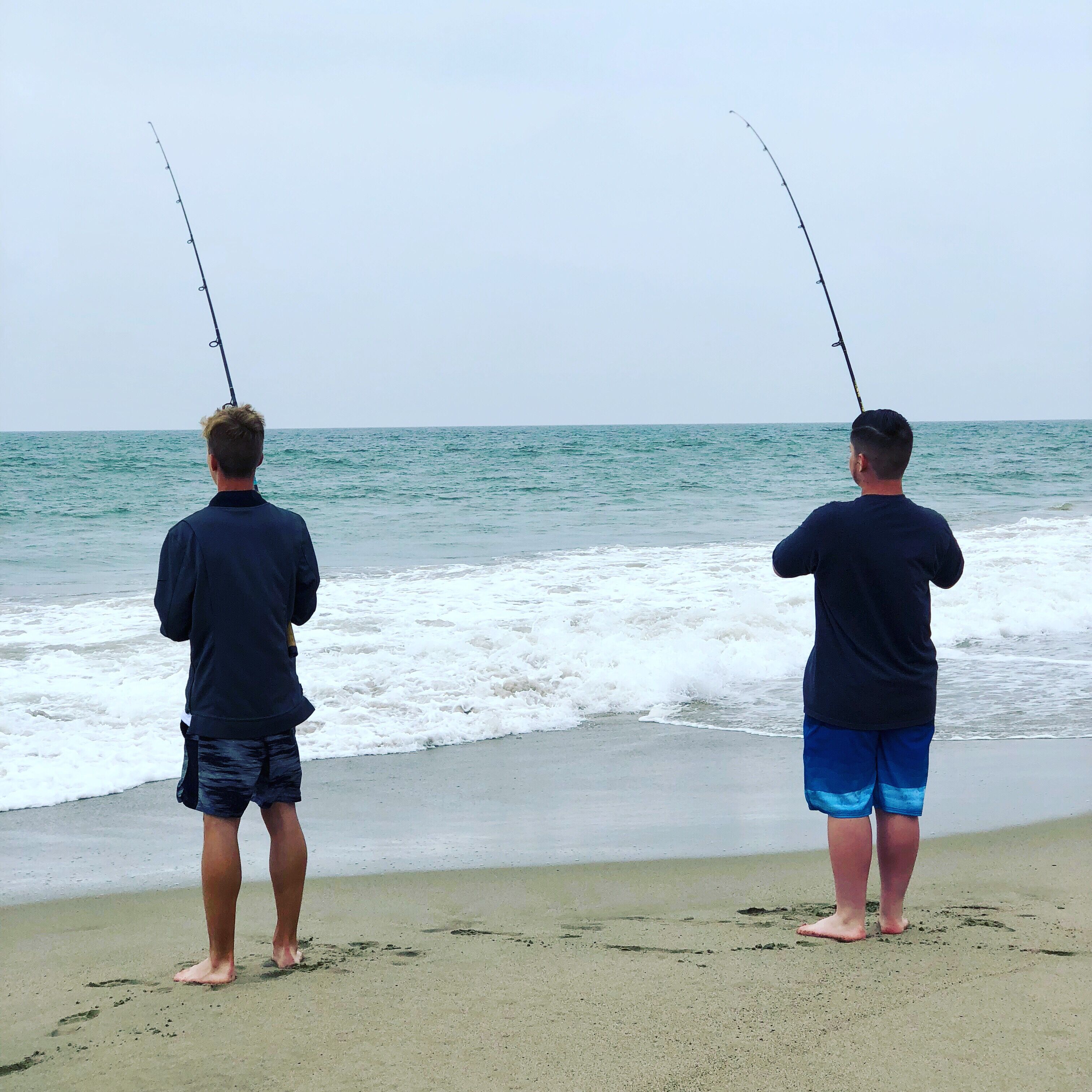 Two individuals fishing on a beach with the ocean in the background.
