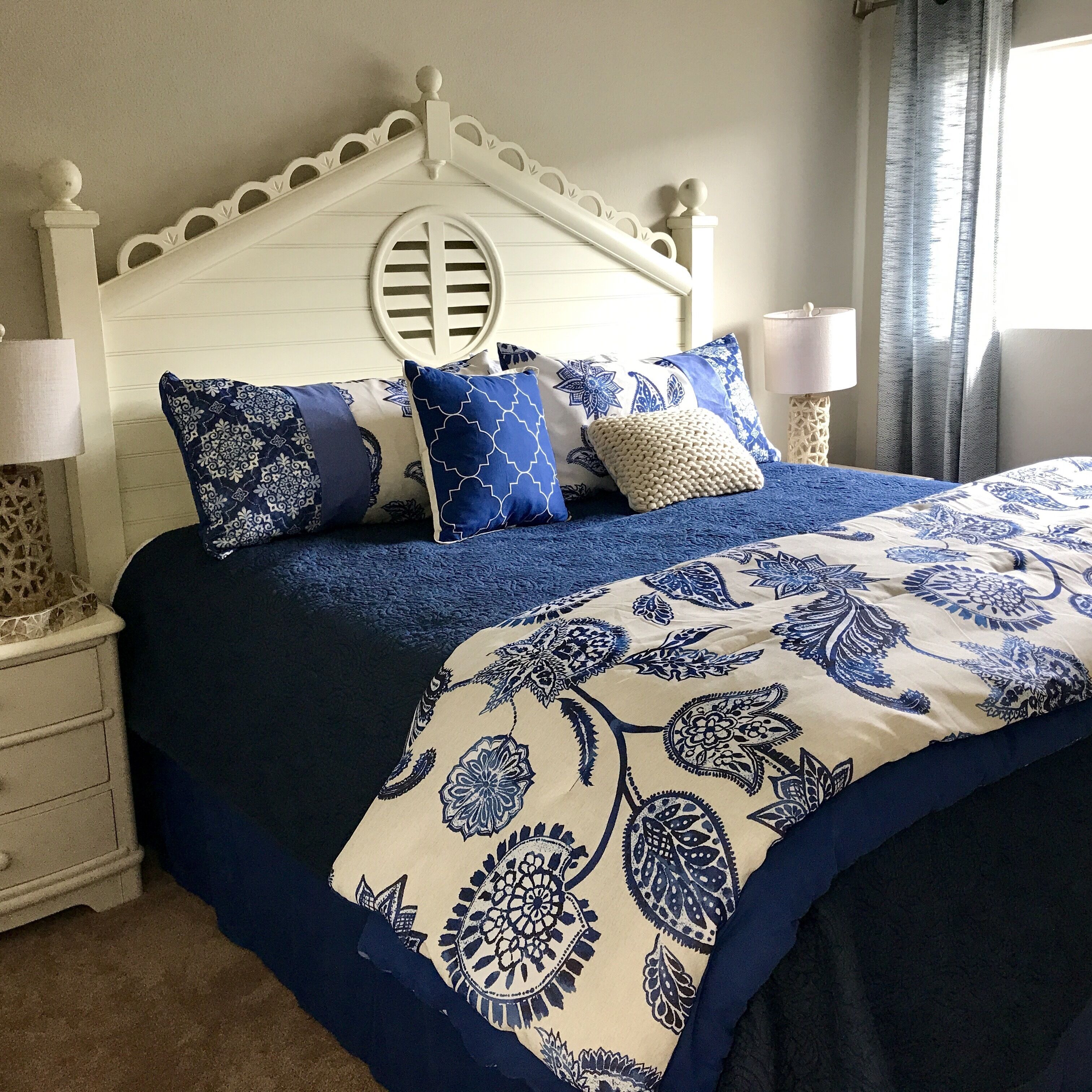 A bed with a blue and white patterned bedspread, white headboard with decorative elements, and multiple pillows with blue and white designs.
