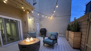 An outdoor patio with a fire pit, two chairs, string lights, a wooden planter, and a view of the house. - Oxnard Beach house two lots from sand! (Oxnard)