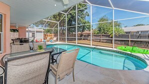 Una piscina cubierta al aire libre con cerramiento de vidrio, ventilador de techo y zona de estar con sillas y una mesa.