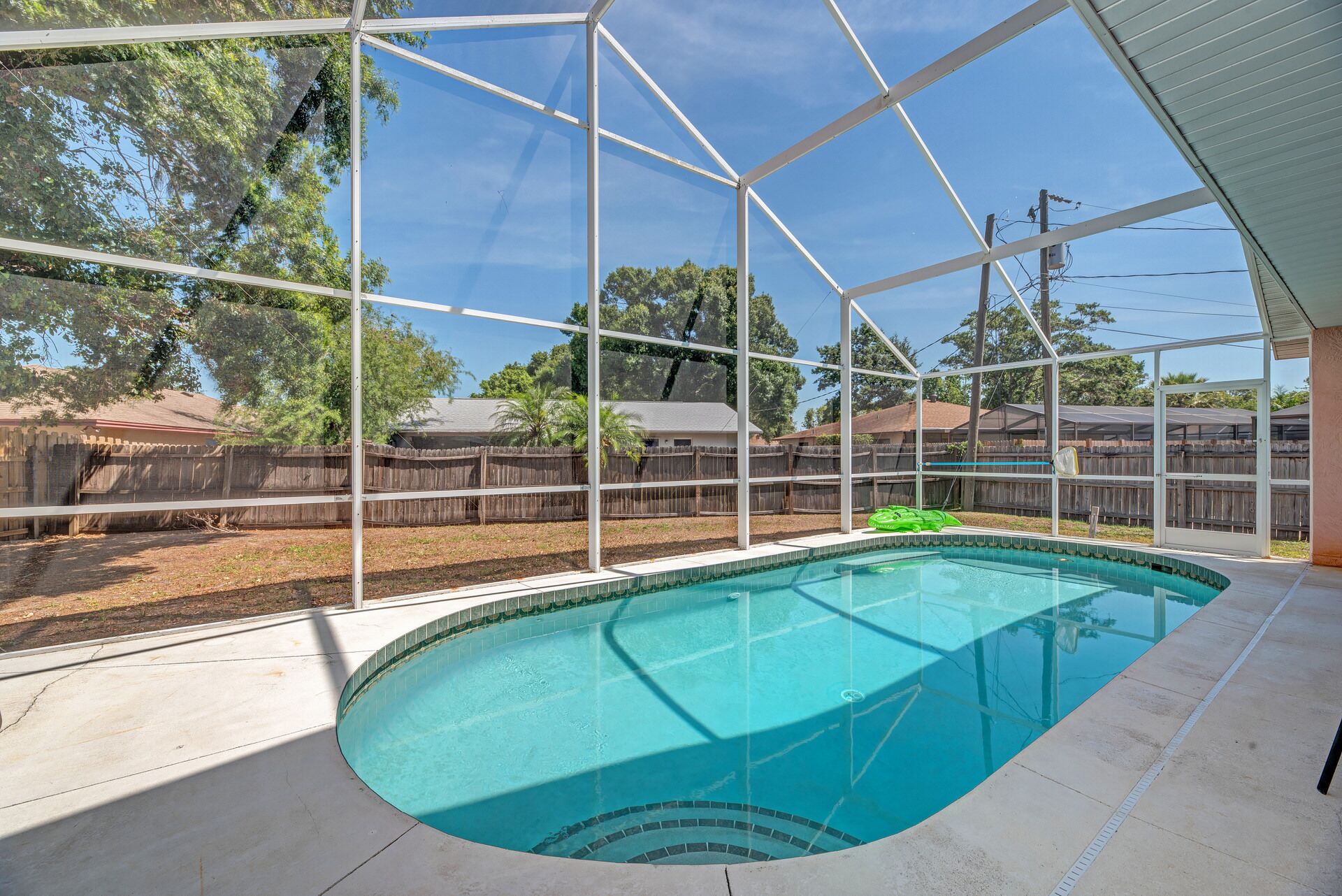 A swimming pool with a clear view of the surrounding area, including a wooden fence and houses in the background.