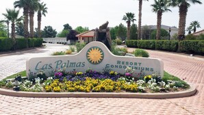 Cartel de Las Palmas Resort Condominiums con un emblema de sol, rodeado de diversas flores coloridas.