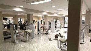 Un gimnasio amplio con diversas máquinas de ejercicio, un espejo grande y piso de baldosas.
