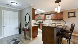 A kitchen with a central island, bar stools, a microwave, and a clock on the wall.