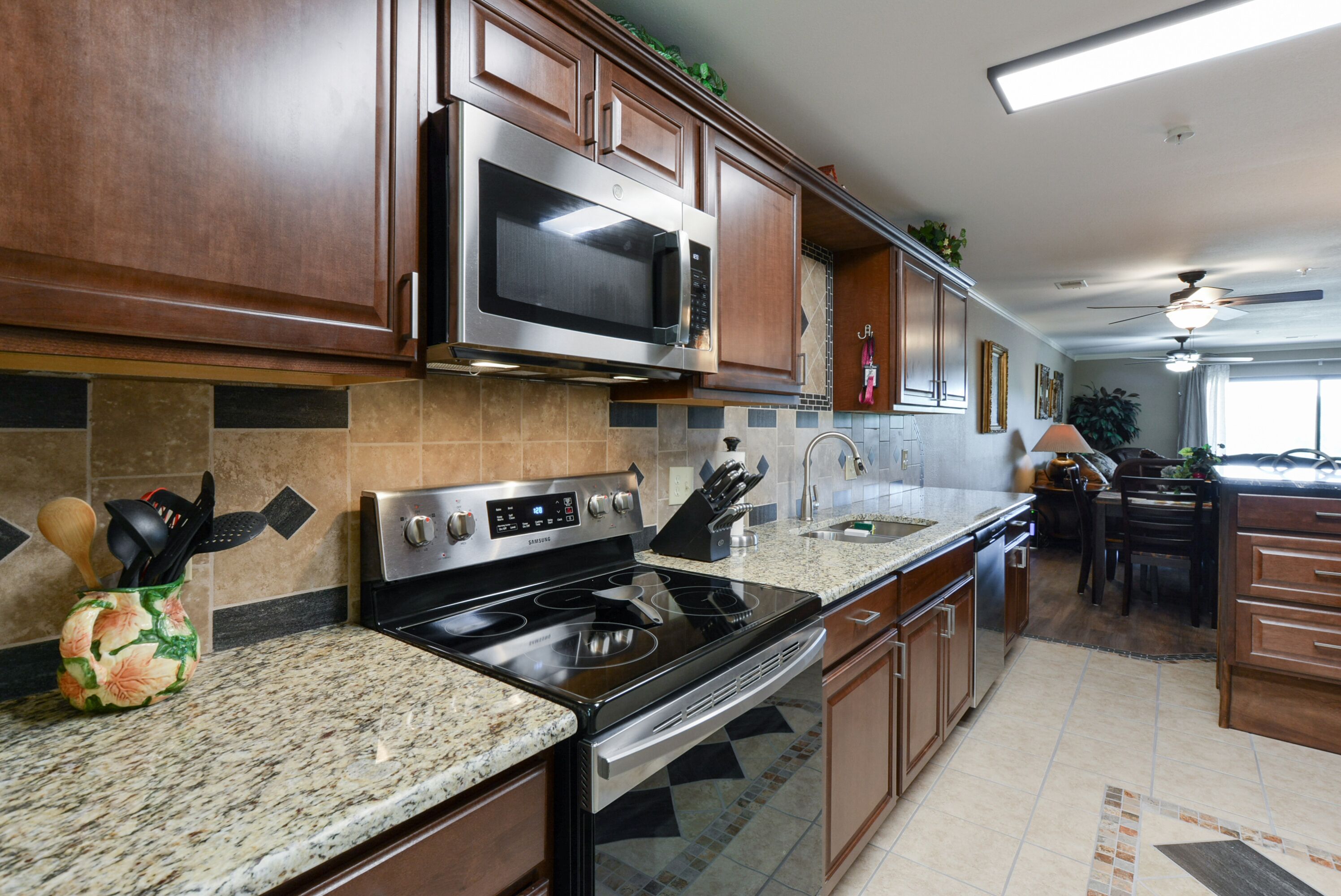A kitchen with wooden cabinets, a stainless steel microwave, a stove, and granite countertops.