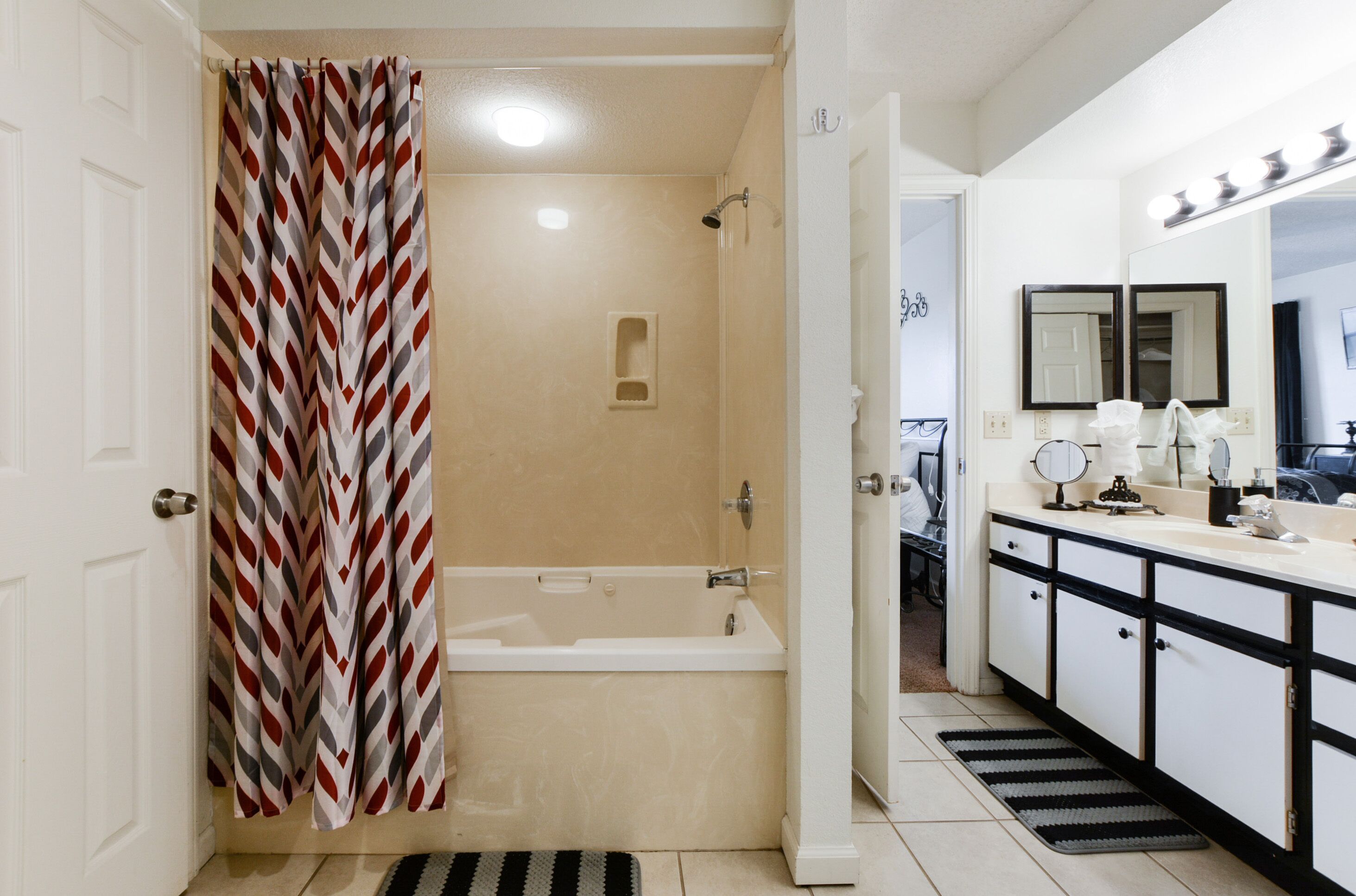 A bathroom with a shower curtain, a bathtub, a vanity with a mirror, and a sink.