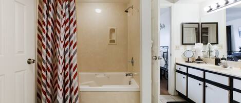 A bathroom with a shower curtain, a bathtub, a vanity with a mirror, and a sink.