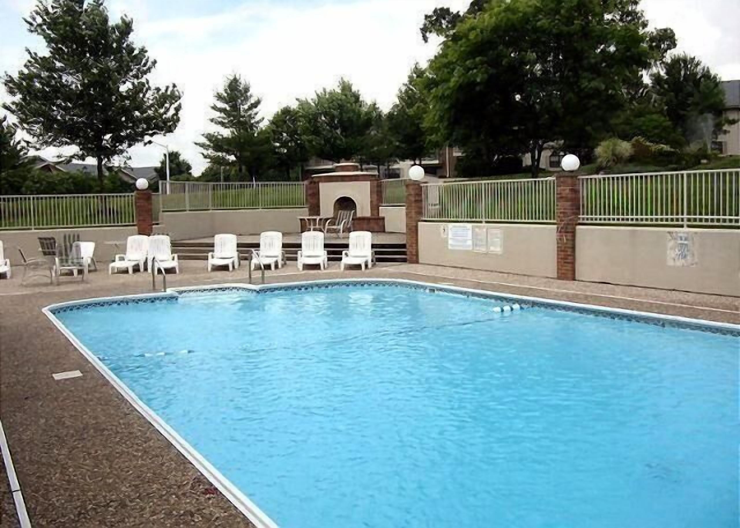 A rectangular swimming pool with a tiled edge, surrounded by white lounge chairs and a brick wall.