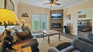 A living room with a fireplace, a ceiling fan, and a view of the outdoors through the glass doors. - STAY NEAR THE STRIP, ONE MINUTE OFF PARKWAY WITH SENSATIONAL VIEWS. (pigeon forge)
