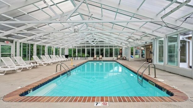 A covered swimming pool with a glass ceiling, surrounded by lounge chairs and a brick border. - STAY NEAR THE STRIP, ONE MINUTE OFF PARKWAY WITH SENSATIONAL VIEWS. (pigeon forge)