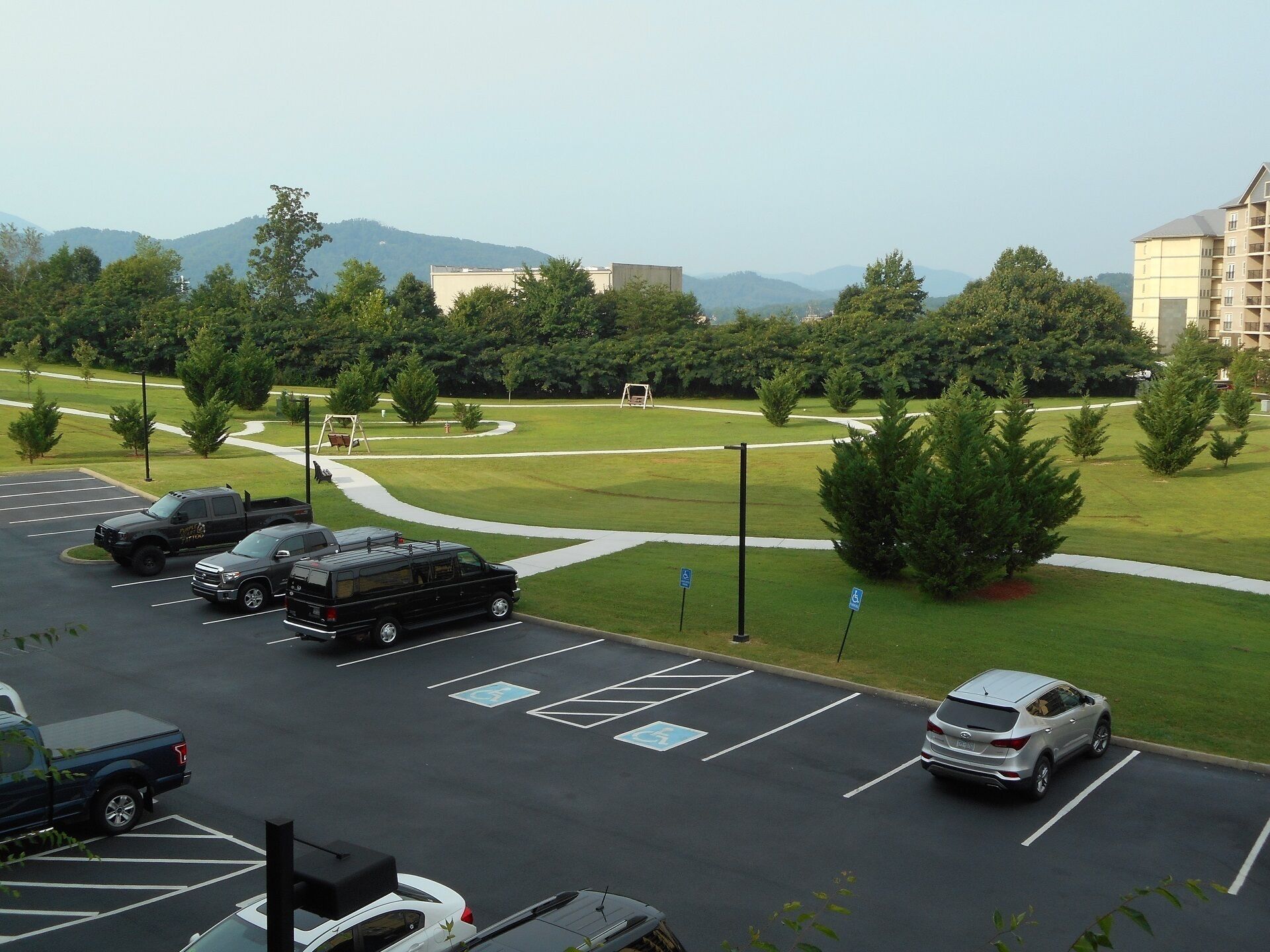 A parking lot with multiple vehicles, including a white car and a black SUV, and a few handicap-accessible parking spaces.