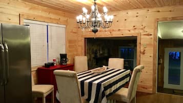 L’intérieur d’un chalet en bois chaleureux et accueillant, avec une table à manger dressée pour quatre personnes, un lustre et une cheminée en pierre.