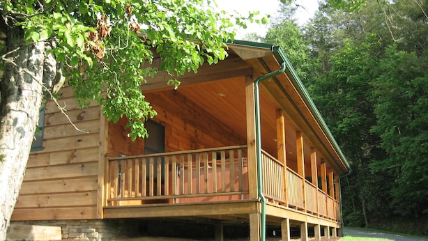 Eine Holzhütte mit Veranda, Stein Fundament und einem grünen Rasen.