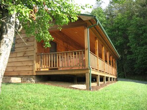 Una cabaña de madera con porche, cimientos de piedra y un patio cubierto de césped.