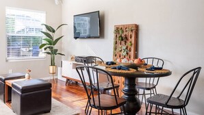 A dining area with a round table, black chairs, a potted plant, and a wall-mounted TV. - Charming Mid-Century Craftsman ~ Hot Tub/Serene Yd (San Diego)