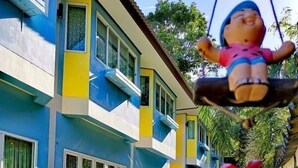 A colorful building with a blue and yellow facade, a swing hanging from a tree, and a small garden area with a chair and potted plants. - Arunee Resort Koh Chang (Ko Chang)