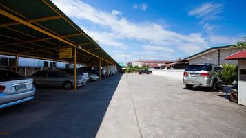 Un estacionamiento con varios coches, una estructura cubierta y edificios al fondo.