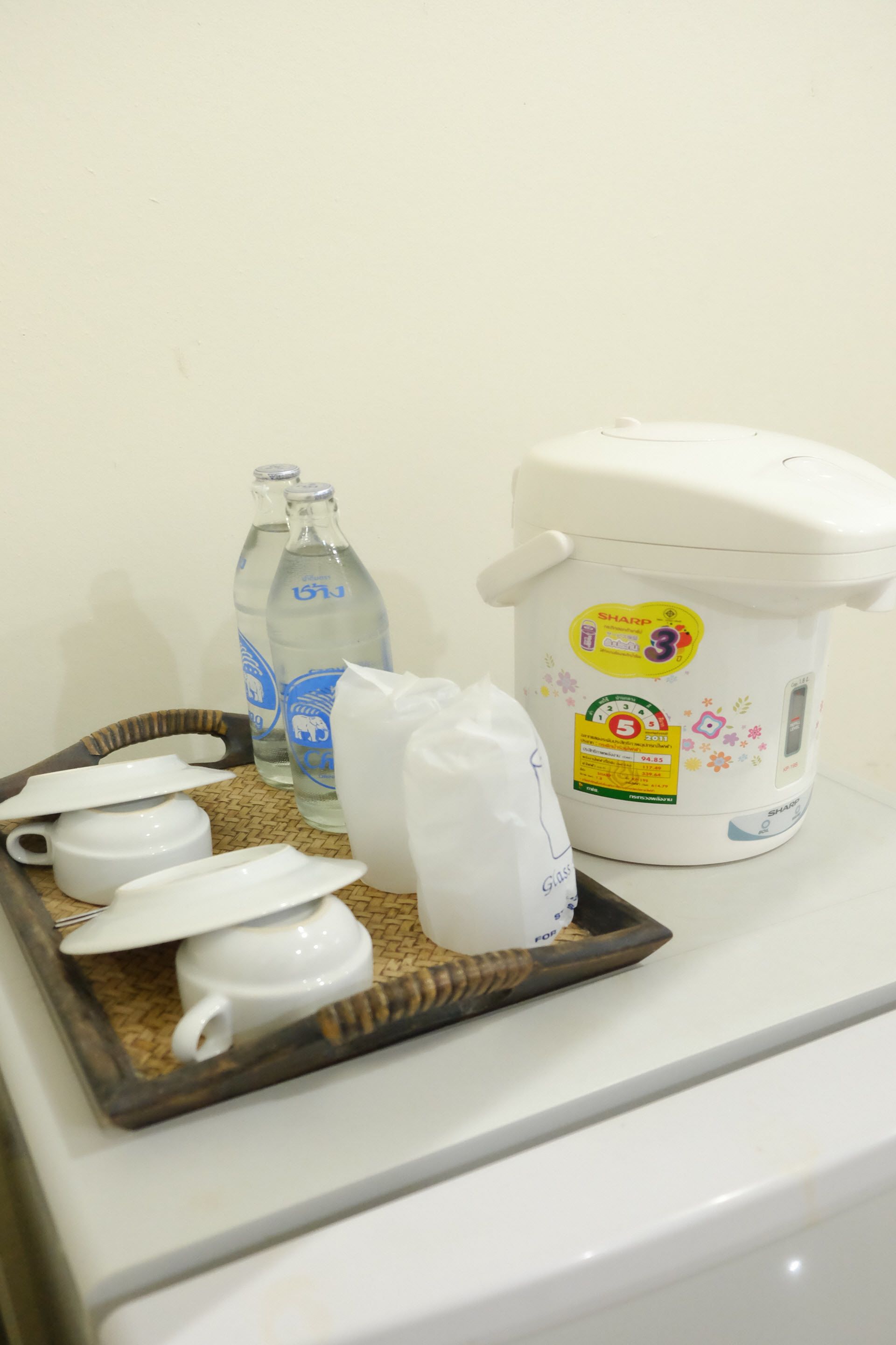 Una zona de cocina con una cocedora de arroz, una botella de agua y una bandeja con tazas blancas y una tetera.