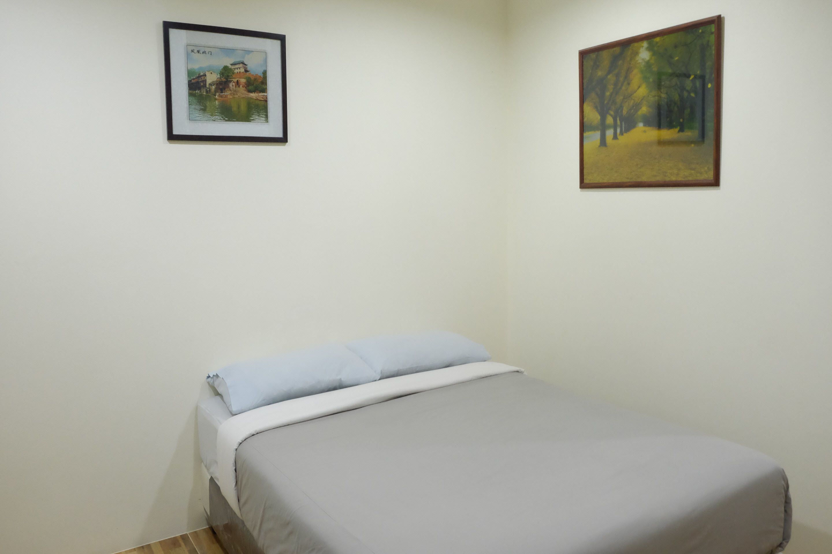 A bedroom with a bed, a framed painting on the wall, and a wooden floor.