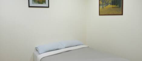 A bedroom with a bed, a framed painting on the wall, and a wooden floor.