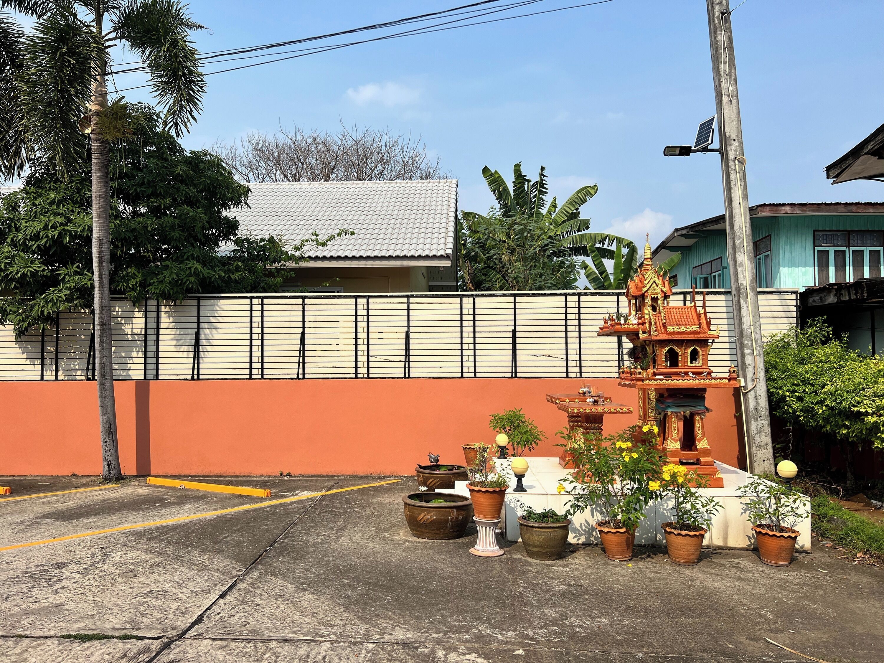 A residential area with a white house, orange wall, and a small shrine with potted plants.