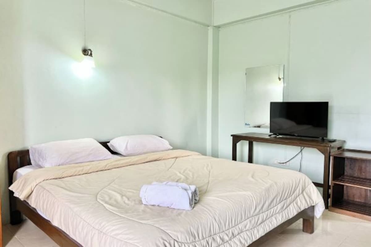 A bedroom with a bed, a television on a wooden table, and a mirror on the wall.