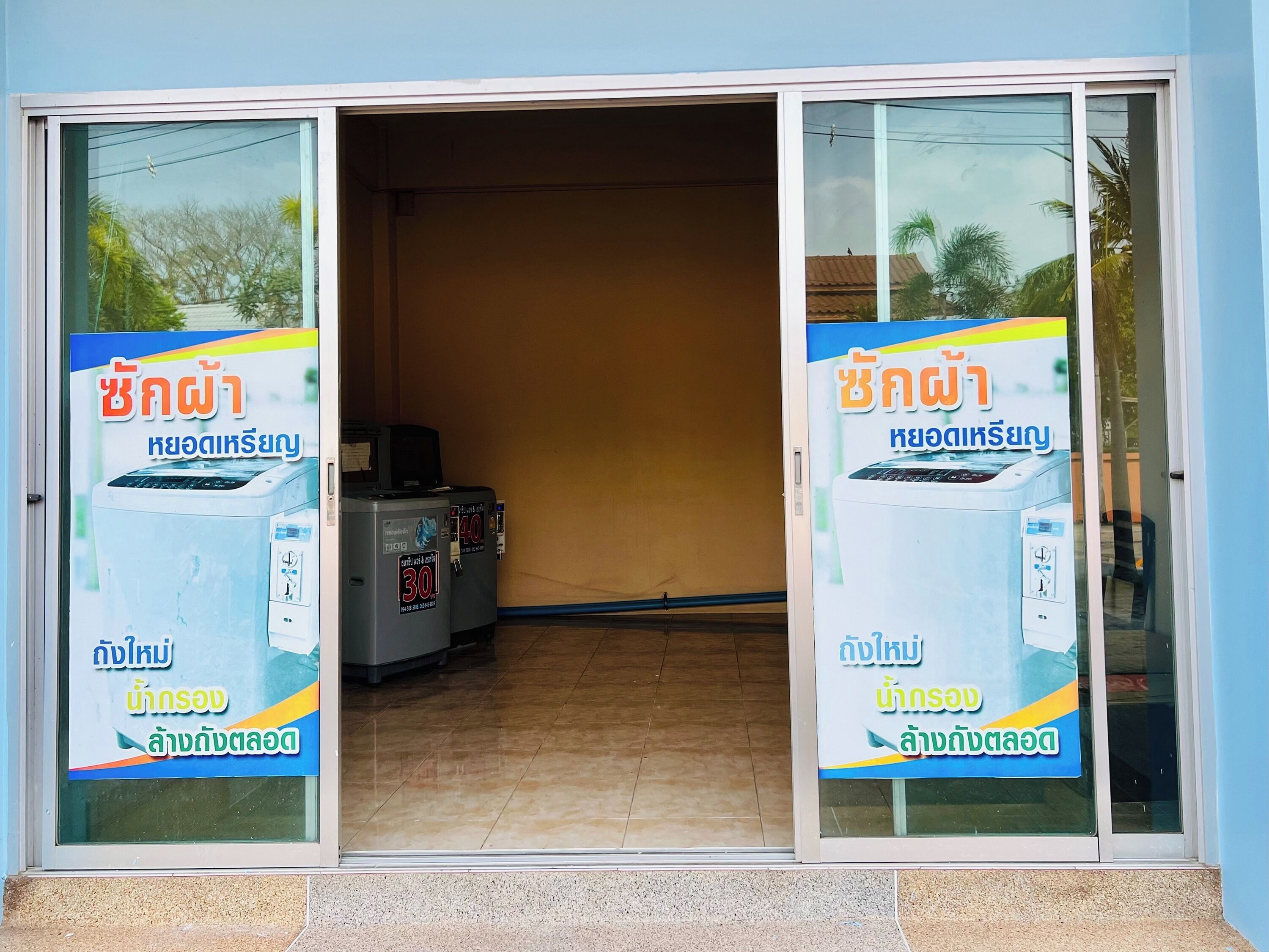 A building entrance with glass doors, a tiled floor, and a poster advertising a washing machine service.