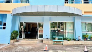 Un edificio de varios pisos con fachada azul, una entrada curva y un banco en el exterior.