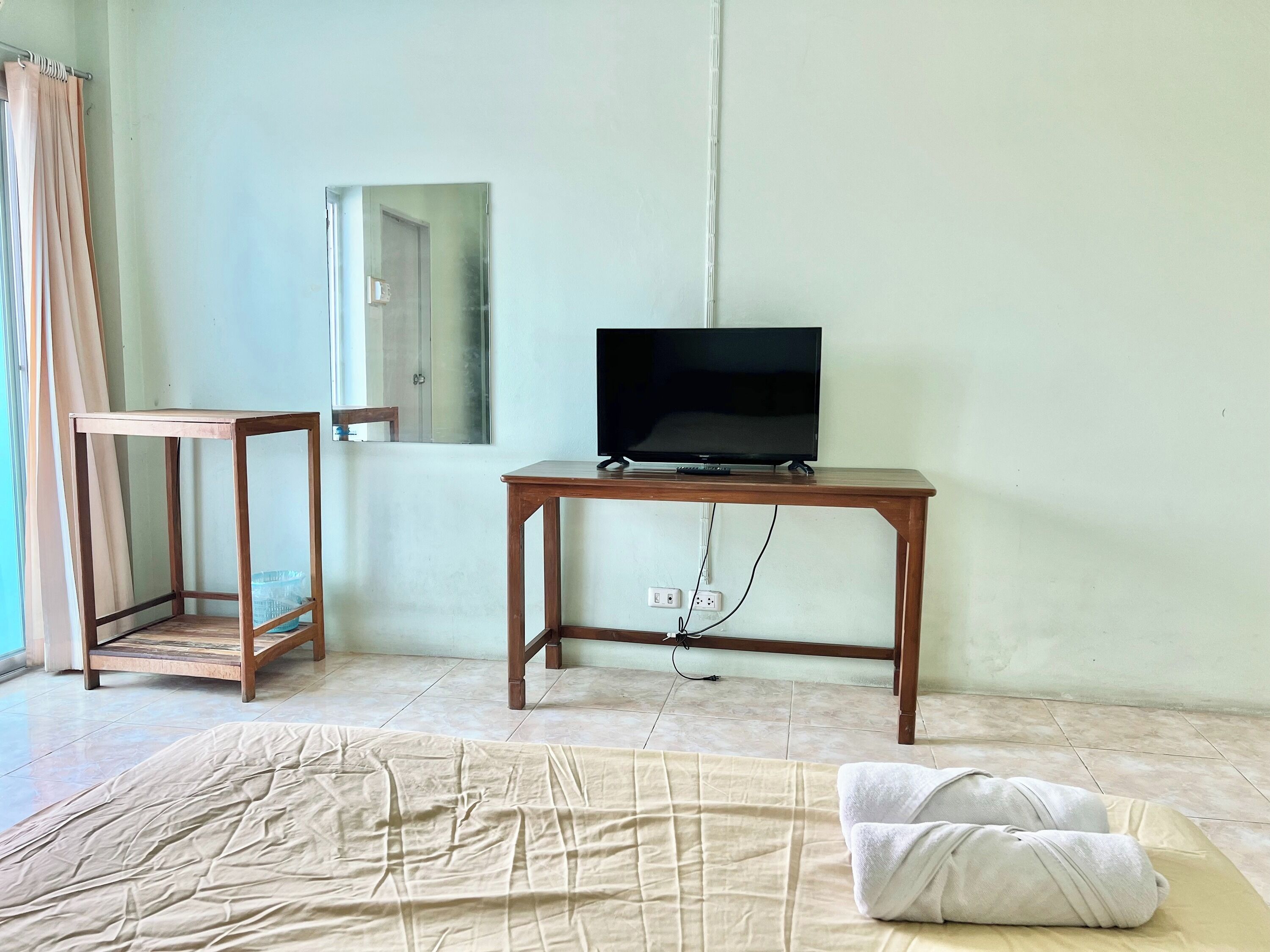 A room with a bed, a TV on a wooden table, a mirror, and a door.