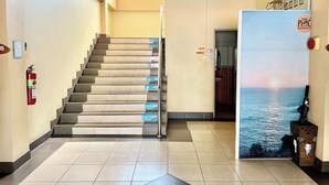 Una escalera con peldaños numerados que conduce a un piso superior, un extintor en la pared y una puerta de baño con señalización de instalaciones diferenciadas por género.