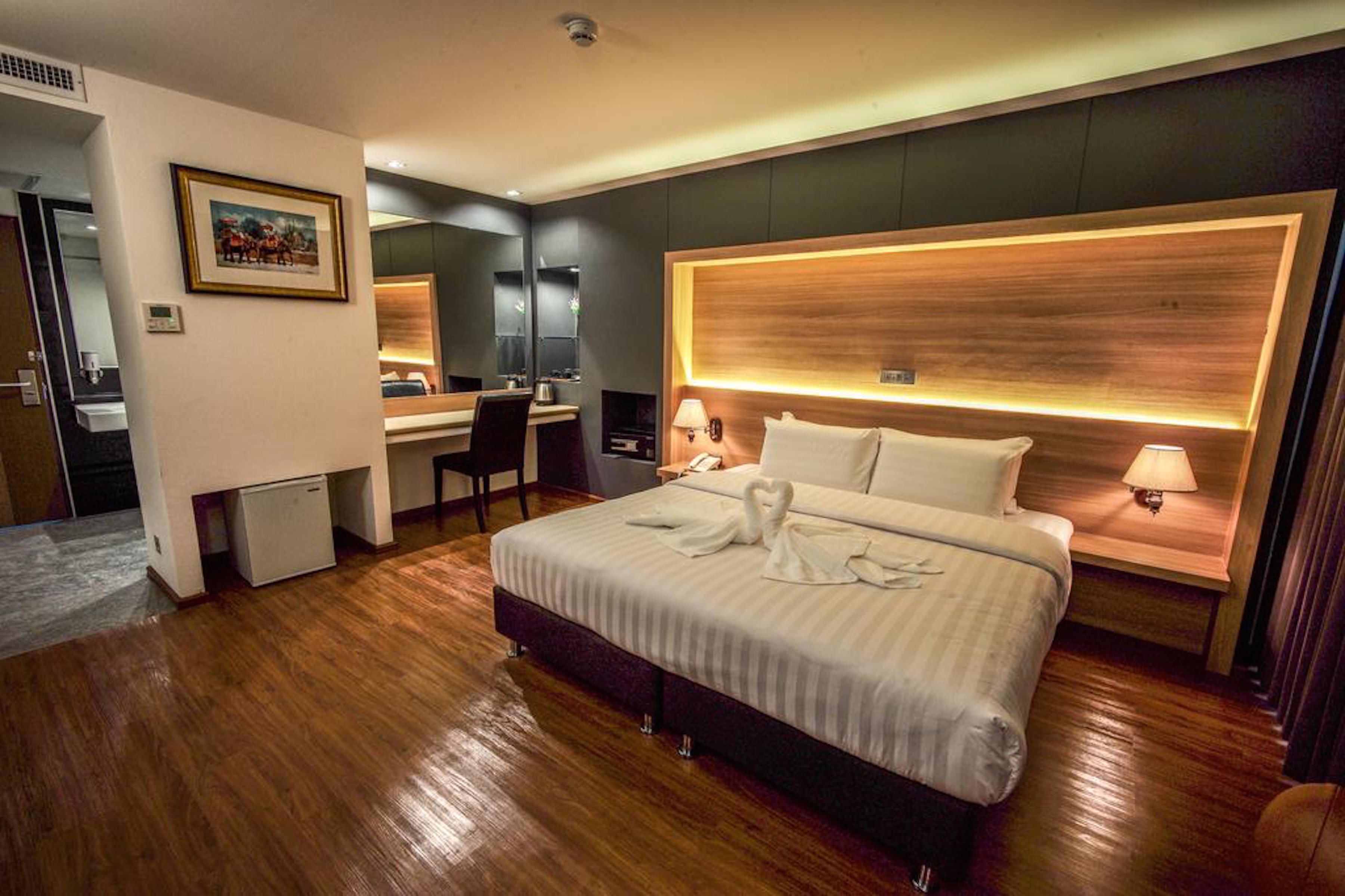 A modern hotel room with a large bed, bedside lamps, a desk, and a small refrigerator.