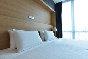 Ein Hotelzimmer mit einem hölzernen Kopfteil, weißer Bettwäsche und Blick ins Freie durch große Fenster.