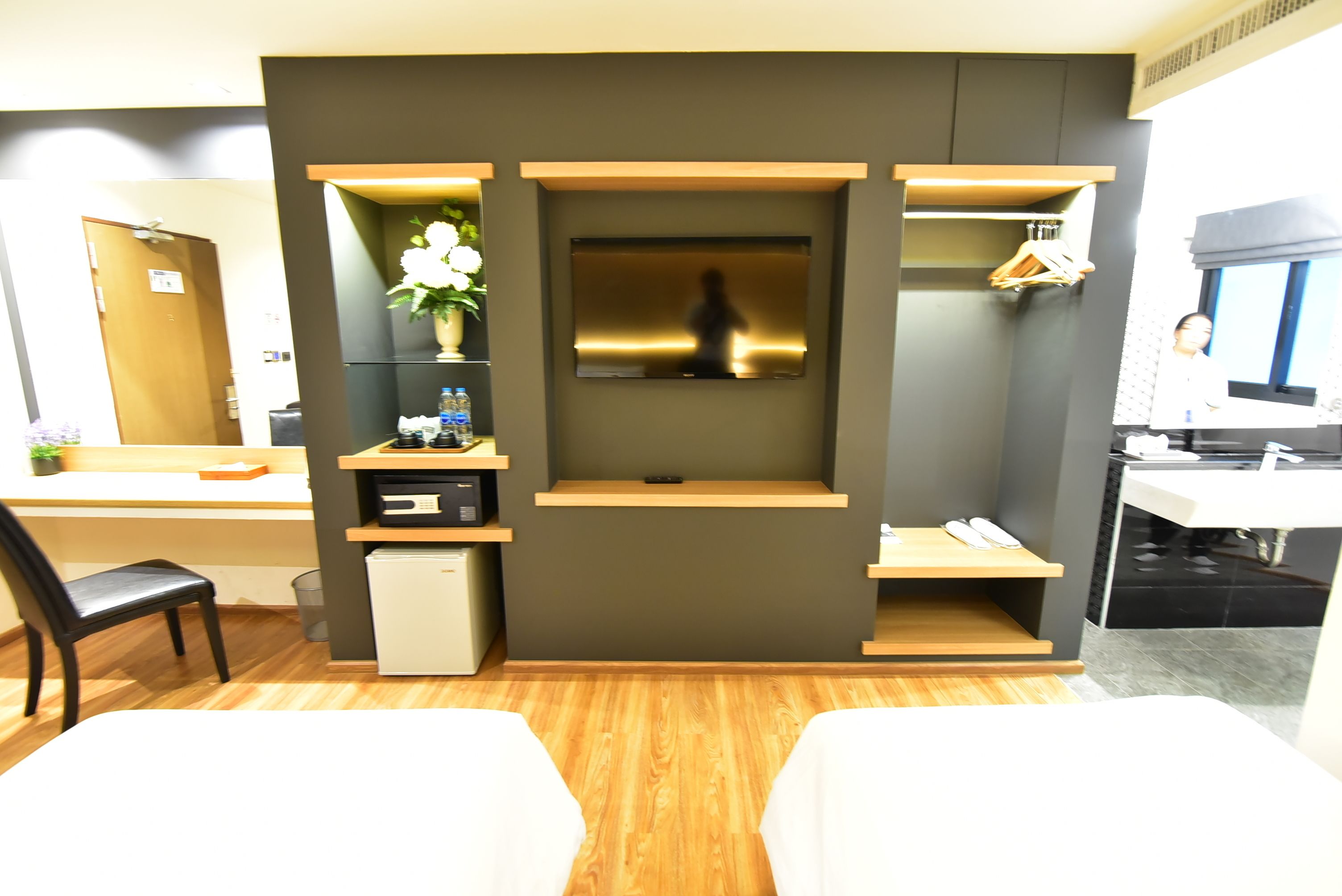 A hotel room with a bed, a desk, a chair, a small refrigerator, a TV, and a mirror.