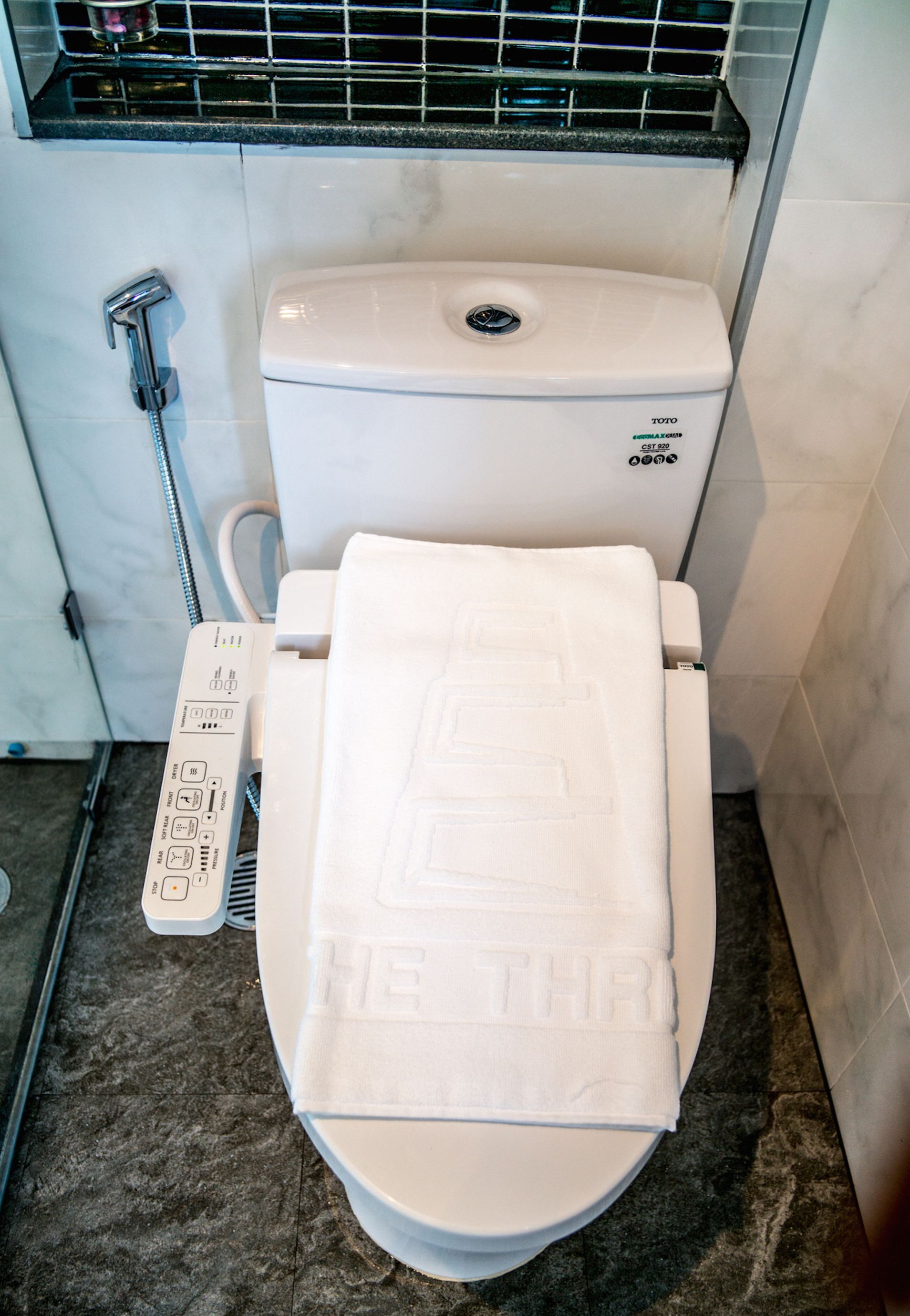 A modern toilet with a control panel and a towel with "HEALTH THRIVE" printed on it.