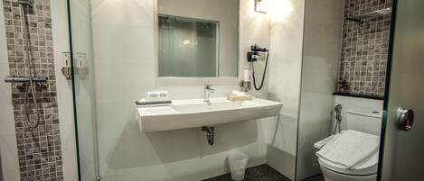 A modern bathroom with a glass shower enclosure, a white sink with a mirror above it, and a toilet with a paper towel holder.